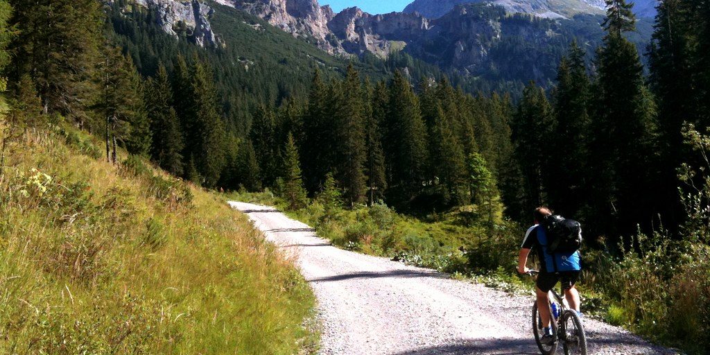 A cyclist on a gravel track below limestone peaks in the Austrian Alps