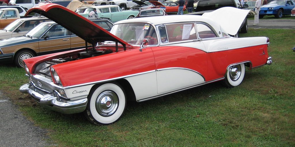 A classic car parked in front of rows of cars at a sale