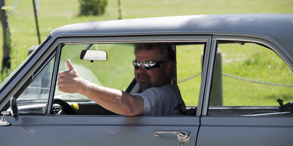 A driver giving a thumbs up from the window of a classic car
