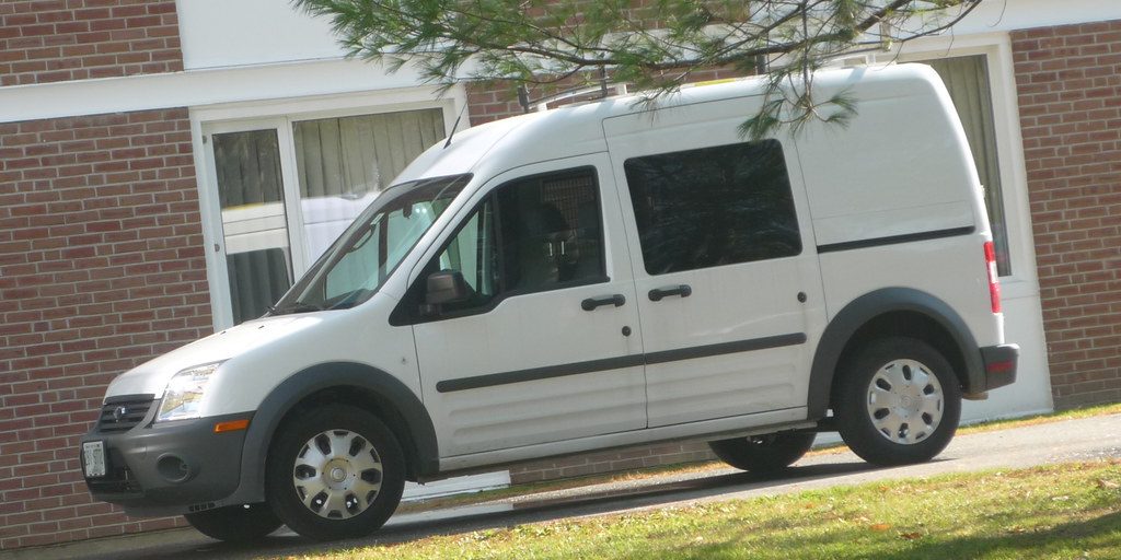 A white company van parked beside a grass verge