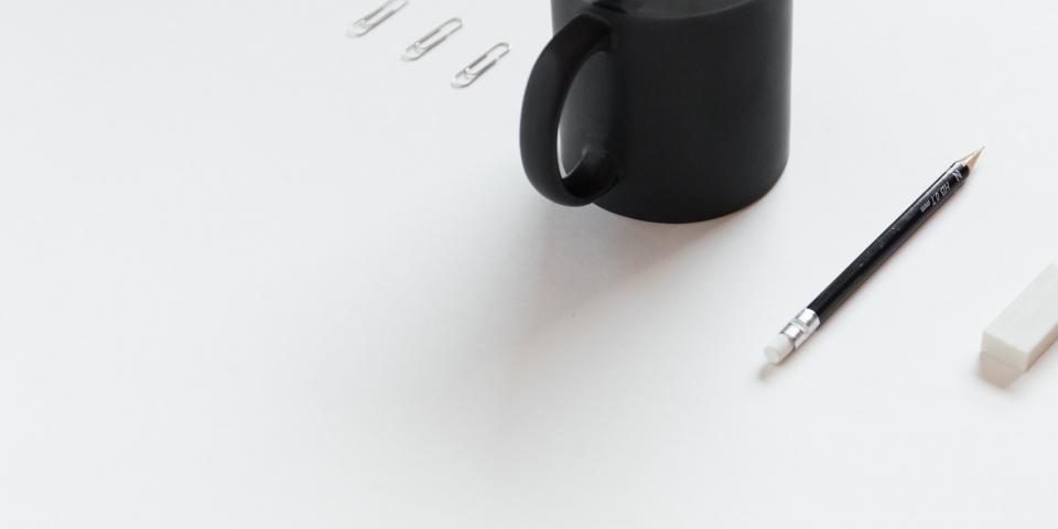 A mug, a pen and paper clips on a white desk